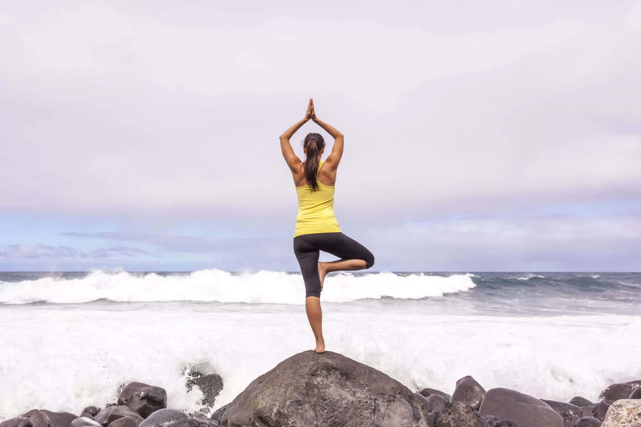 Young woman practicing tree yoga pose near the ocean during sunset